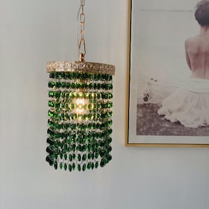 May include: A green crystal chandelier pendant light with a gold metal frame. The light is hanging from a chain.