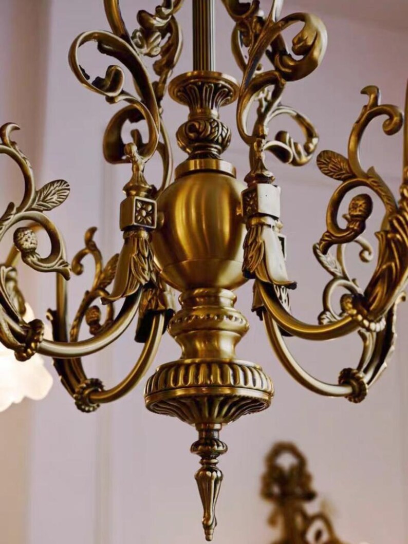 May include: A gold-toned chandelier with ornate, scrolled arms and a central, bulbous, decorative element. The chandelier has a classic, elegant design.
