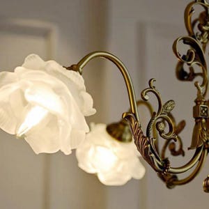 May include: A gold-toned chandelier with ornate detailing and white frosted glass shades shaped like roses.