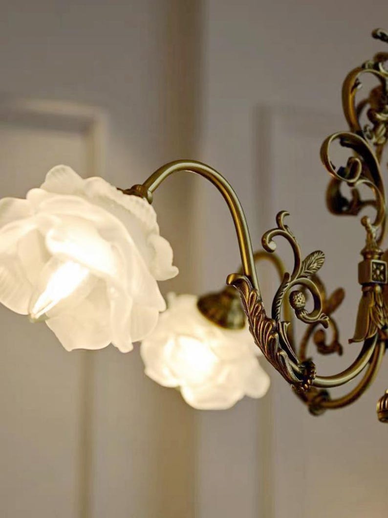 May include: A gold-toned chandelier with ornate detailing and white frosted glass shades shaped like roses.