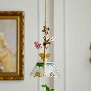 May include: A stained glass pendant light with a white, green, and yellow design. The light fixture is attached to a chain with a floral motif and pink roses.
