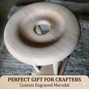May include: A light-colored wooden marudai featuring a smooth, circular top with a central hole. The structure includes vertical supports and a base. The text on the image reads: PERFECT GIFT FOR CRAFTERS Custom Engraved Marudai.