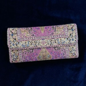 Könnte beinhalten: Eine rechteckige Clutch-Geldbörse mit einem gewebten Gobelinmuster in Magenta, Gold, Schwarz und Blau. Das Design zeigt komplizierte florale und geometrische Motive auf der gesamten Oberfläche, einschließlich der umschlagbaren Verschlussklappe.