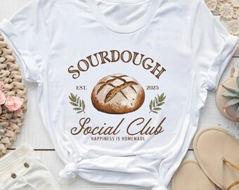 May include: White t-shirt with a brown sourdough bread illustration and the text "Sourdough Social Club Est. 2025 Happiness is Homemade" printed on it.