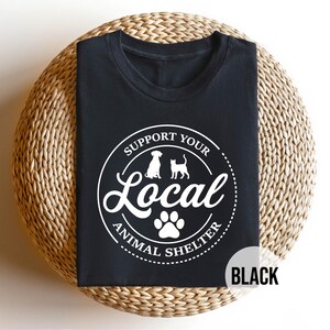 May include: Black t-shirt with a white circle graphic that says "Support Your Local Animal Shelter" with a paw print in the center and silhouettes of a dog and cat.