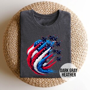 May include: Dark gray heather t-shirt with a graphic of a red, white, and blue American flag with jets flying through it. The text "DARK GRAY HEATHER" is printed on the bottom right corner of the shirt.