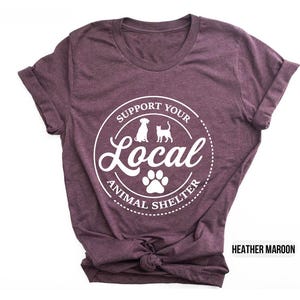 May include: Heather maroon t-shirt with a white circle graphic that says "Support Your Local Animal Shelter" with a paw print and silhouettes of a dog and cat.
