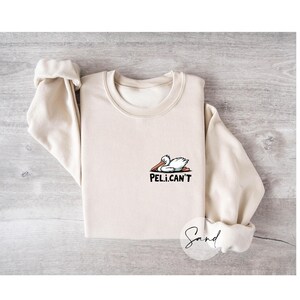 May include: A beige sweatshirt with a cartoon pelican graphic and the text "PEL.I.CAN'T".