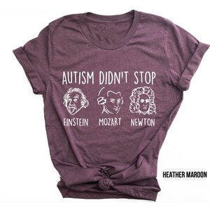 Pu&ograve; includere: T-shirt color marrone rossiccio con testo bianco che recita "L'autismo non si &egrave; fermato" e presenta illustrazioni di Albert Einstein, Mozart e Isaac Newton. Il testo sotto le illustrazioni recita "Einstein, Mozart, Newton."