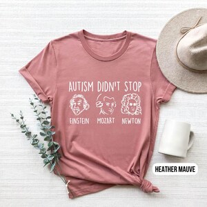 Pu&ograve; includere: T-shirt color malva heather con il testo "L'autismo non si &egrave; fermato" e immagini di Einstein, Mozart e Newton.