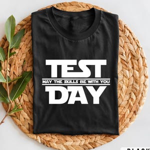 May include: Black t-shirt with white text that reads "TEST MAY THE SKILLS BE WITH YOU DAY".