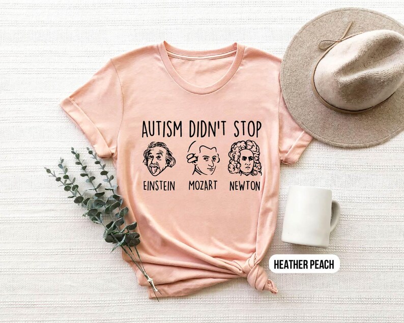Pu&ograve; includere: Una maglietta rosa con il testo "L'autismo non ha fermato" e immagini di Einstein, Mozart e Newton. La maglietta &egrave; disponibile in pesca brughiera.