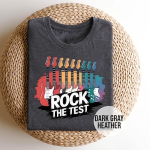 May include: Dark gray heather t-shirt with a graphic of colorful electric guitars and the text "Rock the Test".