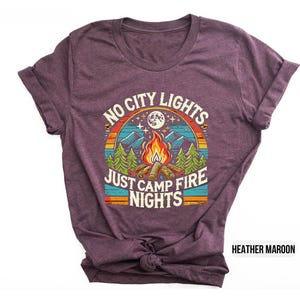 K&ouml;nnte beinhalten: T-Shirt in Heidekraut-Maroon mit einem Retro-Grafikdesign mit einem Lagerfeuer, B&auml;umen und dem Text "No City Lights Just Camp Fire Nights".