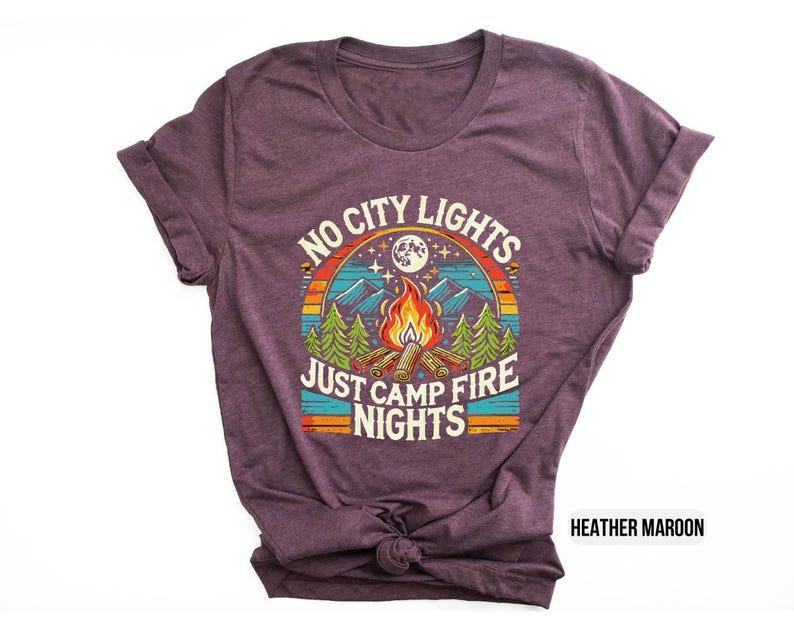 K&ouml;nnte beinhalten: T-Shirt in Heidekraut-Maroon mit einem Retro-Grafikdesign mit einem Lagerfeuer, B&auml;umen und dem Text "No City Lights Just Camp Fire Nights".