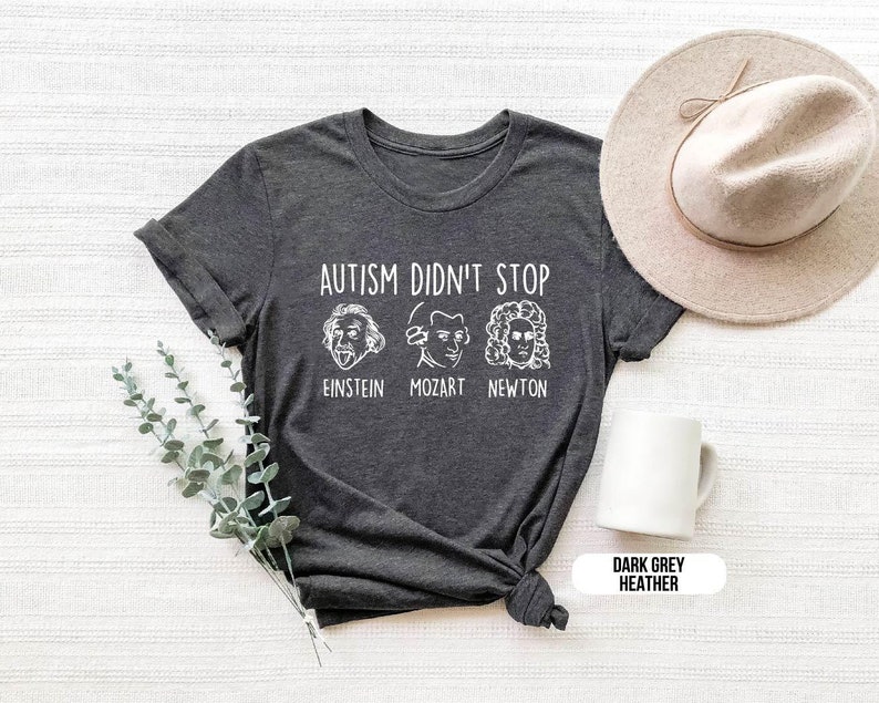 Pu&ograve; includere: Maglietta in grigio scuro melange con il testo "L'autismo non si &egrave; fermato" e illustrazioni di Albert Einstein, Mozart e Isaac Newton. Il testo sotto le illustrazioni recita "Einstein, Mozart, Newton".