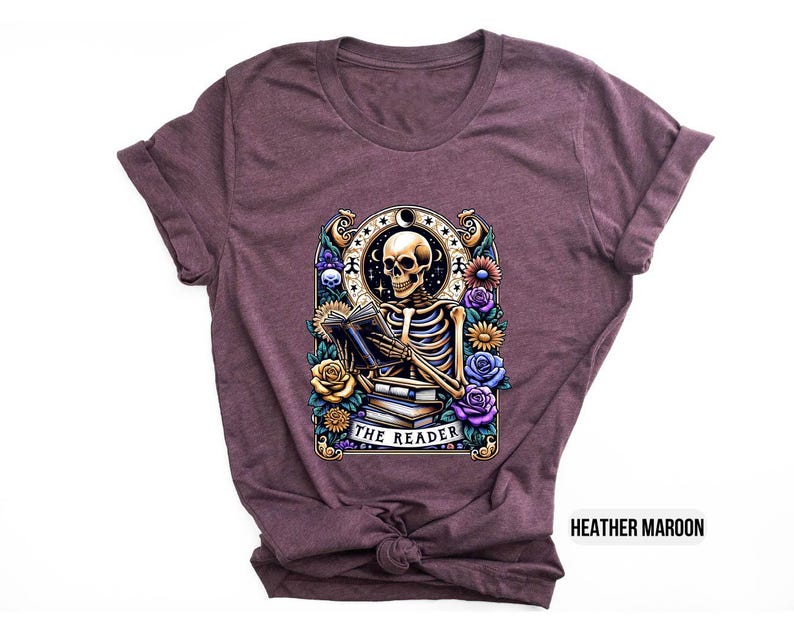 May include: A heather maroon t-shirt with a graphic of a skeleton reading a book surrounded by flowers. The text "The Reader" is printed below the skeleton.