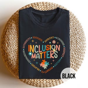 May include: Black t-shirt with a colorful graphic that says "Inclusion Matters" surrounded by words like "diversity", "empathy", "kindness", and "respect".