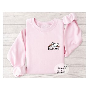 May include: A light pink sweatshirt with a cartoon pelican and the text "PEL.I.CAN'T" printed on the front.