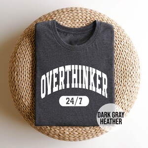 Peut inclure: T-shirt gris chin&eacute; fonc&eacute; avec du texte blanc qui dit "Overthinker 24/7".
