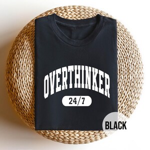 Peut inclure: T-shirt noir avec du texte blanc qui dit "Overthinker 24/7".