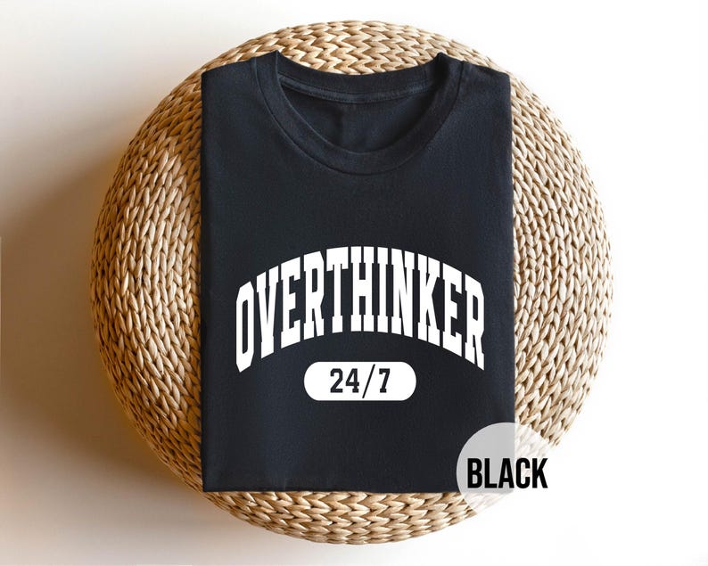 Peut inclure: T-shirt noir avec du texte blanc qui dit "Overthinker 24/7".