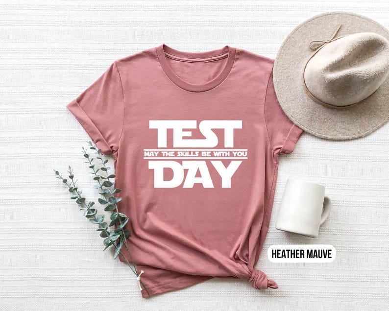 K&ouml;nnte beinhalten: Ein T-Shirt in Heide-Mauve mit dem Text "TEST MAY THE SKILLS BE WITH YOU DAY" in Wei&szlig;.