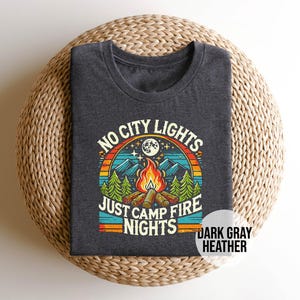 K&ouml;nnte beinhalten: Dunkelgraues T-Shirt aus Heather-Material mit einem Retro-Grafikdesign, das ein Lagerfeuer, Berge und den Text "No City Lights Just Camp Fire Nights" zeigt.
