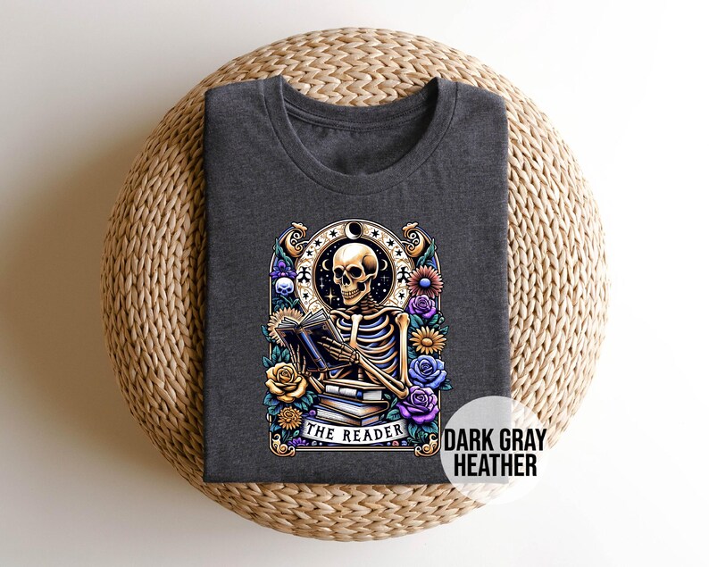 May include: Dark gray heather t-shirt with a graphic of a skeleton reading a book surrounded by flowers. The text "The Reader" is below the skeleton.