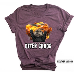 May include: A heather maroon t-shirt with a graphic of an otter in a fiery explosion. The text "Otter Chaos" is printed in white below the graphic.