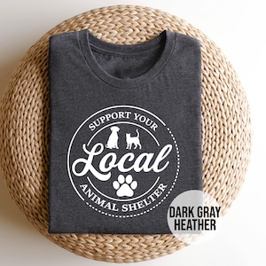 May include: Dark gray heather t-shirt with a white circle graphic that says "Support Your Local Animal Shelter" with a paw print and silhouettes of a dog and cat.