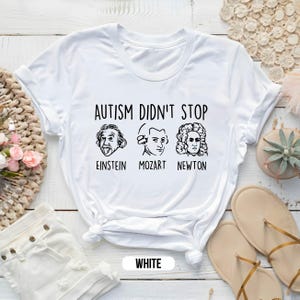 Pu&ograve; includere: Maglietta bianca con il testo "L'autismo non ha fermato" e immagini di Albert Einstein, Mozart e Isaac Newton. Il testo sotto le immagini dice "Einstein, Mozart, Newton".