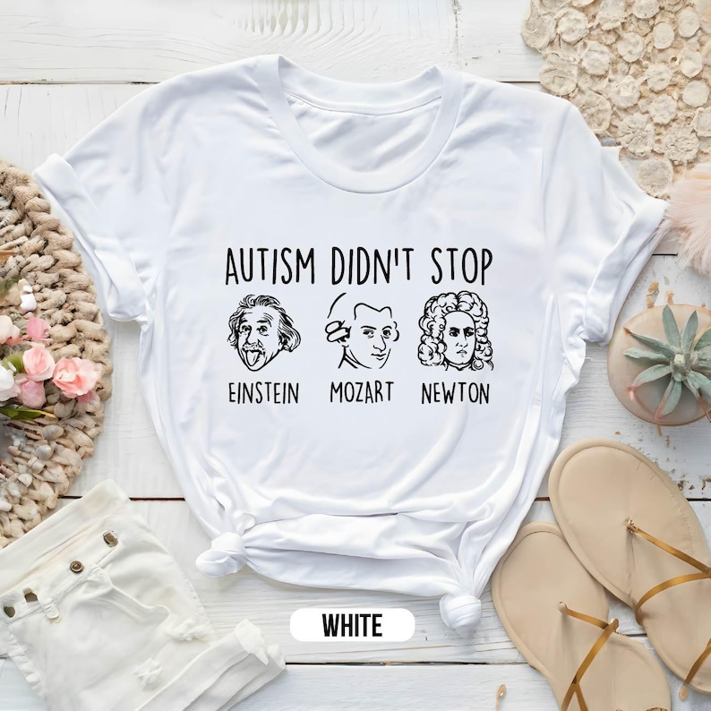 Pu&ograve; includere: Maglietta bianca con il testo "L'autismo non ha fermato" e immagini di Albert Einstein, Mozart e Isaac Newton. Il testo sotto le immagini dice "Einstein, Mozart, Newton".