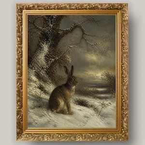 May include: A framed oil painting depicting a brown hare sitting on a snow-covered hillside. The scene includes a large, dark, snow-dusted tree on the left and a moody, overcast winter sky in the background. The artwork is encased in an ornate gold frame.