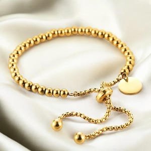 May include: A gold beaded bracelet with a round charm and an adjustable sliding clasp.