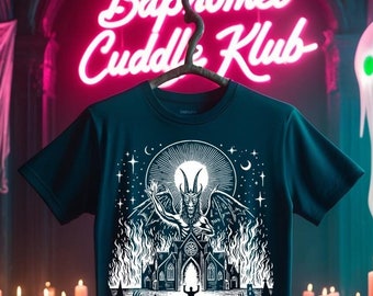 May include: A dark blue t-shirt with a white graphic of a horned figure standing in front of a burning church. The text "Baphomet Cuddle Klub" is in pink neon letters above the shirt.