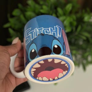 May include: Blue ceramic mug featuring the character Stitch from Lilo & Stitch. The mug has a white handle and the word "STITCH!" in white lettering. The design includes Stitch's face and open mouth.