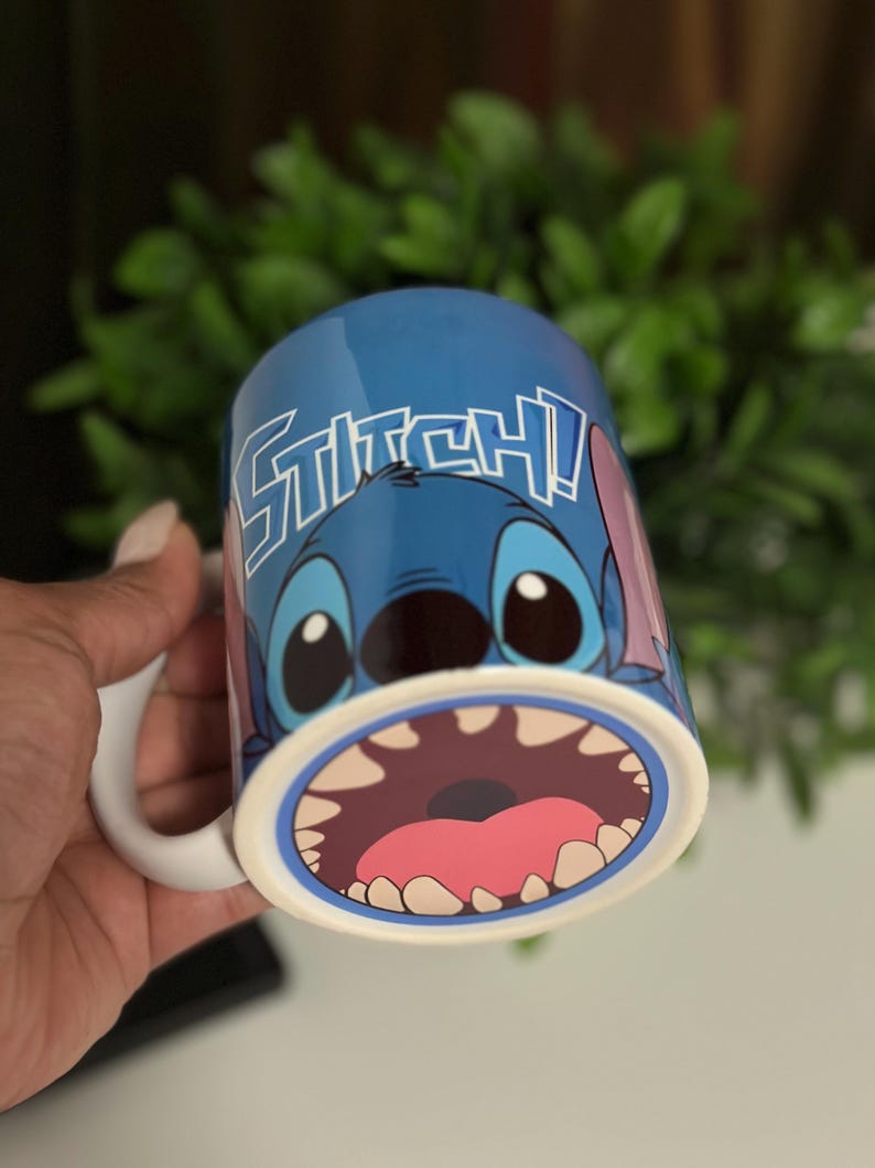 May include: Blue ceramic mug featuring the character Stitch from Lilo & Stitch. The mug has a white handle and the word "STITCH!" in white lettering. The design includes Stitch's face and open mouth.