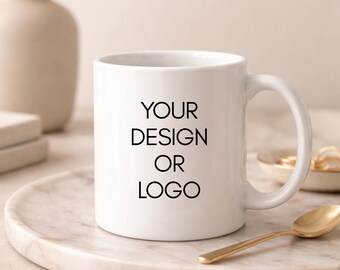 May include: A white ceramic mug featuring the black printed text YOUR DESIGN OR LOGO on the front. The mug has a standard cylindrical shape with a curved handle on the right side, presented as a blank template for custom branding or graphic designs.