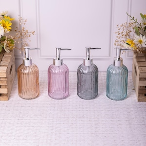 Può includere: Quattro dispenser di sapone in vetro con design a coste in diversi colori: marrone chiaro, rosa, grigio e blu chiaro. Ogni dispenser ha una pompa argentata.