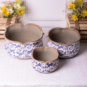 May include: A set of three ceramic plant pots with a blue and white floral design. The pots have a scalloped edge and a neutral interior. The largest pot is approximately 30 cm in diameter.