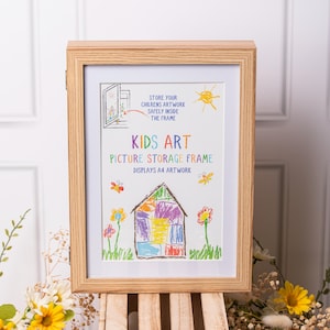 May include: A wooden picture frame with a white mat and a colorful drawing of a house inside. The frame has the text "Kids Art Picture Storage Frame" and "Displays A4 Artwork".