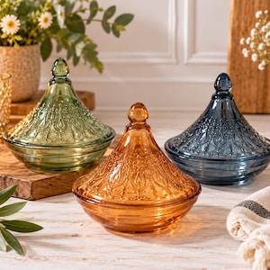 May include: Three glass lidded bowls in green, amber, and blue. Each bowl features a conical lid with a pointed finial and an intricate embossed teardrop pattern. The bowls have a wide, shallow base and a smooth, translucent glass finish.