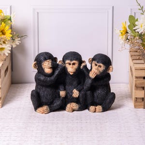 May include: A set of three black monkey figurines in the classic "See no evil, hear no evil, speak no evil" pose. The monkeys are sitting, with detailed facial features and fur texture. Decorative home decor.