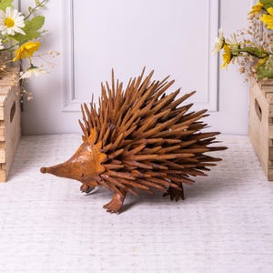 May include: A rustic metal hedgehog sculpture with a textured, spiky body and a pointed snout. The sculpture is a warm, rusty brown color, with visible weld marks. The hedgehog has small, detailed feet and is posed in a walking position. This decorative piece adds a touch of nature to any space.