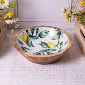 Op de afbeelding: Een houten kom met een witte binnenkant met een citroen- en bladerontwerp. De kom heeft een natuurlijke houtnerf aan de buitenkant en een ronde vorm. Het interieurontwerp omvat gele citroenen en groene bladeren.