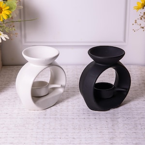 May include: Two ceramic oil diffusers, one white and one black, with a circular opening in the middle. Both diffusers have a small dish for wax melts.