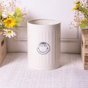 May include: White metal bin with a silver lid and a silver label that reads "The Art of the Bin - A Place for Your Treasures".
