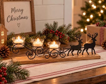 May include: A black metal candle holder featuring a sleigh design pulled by two reindeer silhouettes, mounted on a rectangular wooden base. The holder includes three clear glass votive cups, each containing a lit white tea light candle.
