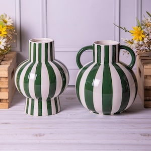 May include: Two ceramic vases with a green and white striped design. One vase has a rounded body and a pedestal base, the other has a similar shape with two curved handles. Both have a glossy finish.